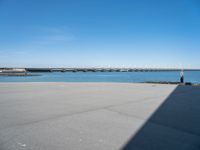 empty street with bridge in distance, on sunny day with clear sky over water and a long concrete walkway in front of it