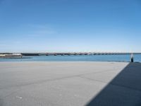 empty street with bridge in distance, on sunny day with clear sky over water and a long concrete walkway in front of it