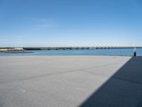 empty street with bridge in distance, on sunny day with clear sky over water and a long concrete walkway in front of it