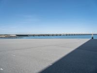 empty street with bridge in distance, on sunny day with clear sky over water and a long concrete walkway in front of it