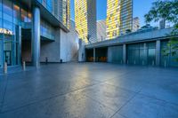 a concrete area with buildings and sky in the background at dusk, including two glass skyscrapers