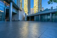 a concrete area with buildings and sky in the background at dusk, including two glass skyscrapers