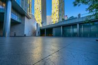 a concrete area with buildings and sky in the background at dusk, including two glass skyscrapers