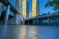 a concrete area with buildings and sky in the background at dusk, including two glass skyscrapers