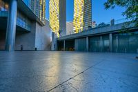 a concrete area with buildings and sky in the background at dusk, including two glass skyscrapers