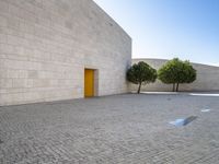 the white bricked courtyard is outside next to trees and small bushes that are beside the wall with a yellow door