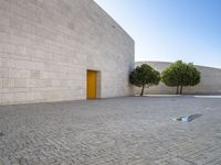 the white bricked courtyard is outside next to trees and small bushes that are beside the wall with a yellow door