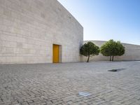 the white bricked courtyard is outside next to trees and small bushes that are beside the wall with a yellow door