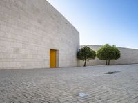 the white bricked courtyard is outside next to trees and small bushes that are beside the wall with a yellow door