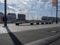 the bench is on a brick area near the water and buildings with sailboats docked in the background