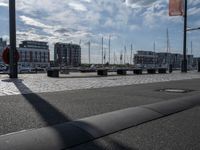 the bench is on a brick area near the water and buildings with sailboats docked in the background