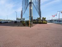 a glass walled building next to cars in front of some flags and buildings with windows