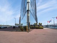 a glass walled building next to cars in front of some flags and buildings with windows