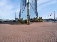 a glass walled building next to cars in front of some flags and buildings with windows