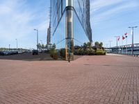 a glass walled building next to cars in front of some flags and buildings with windows