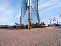 a glass walled building next to cars in front of some flags and buildings with windows