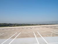 an empty parking lot near a fenced in area with concrete blocks and trees in the background