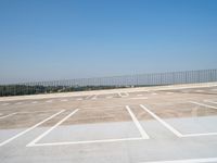 an empty parking lot near a fenced in area with concrete blocks and trees in the background