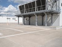 an empty parking lot with stairs going up to an industrial area, with a sky background