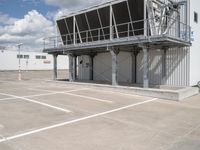 an empty parking lot with stairs going up to an industrial area, with a sky background