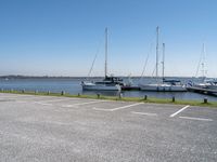 a parking lot with lots of boats on the water behind it and one of the parked cars on the shore