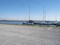 a parking lot with lots of boats on the water behind it and one of the parked cars on the shore