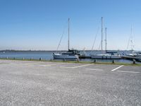 a parking lot with lots of boats on the water behind it and one of the parked cars on the shore