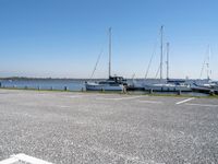 a parking lot with lots of boats on the water behind it and one of the parked cars on the shore