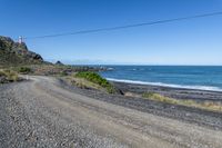 a gravel road going into the ocean with mountains in the background and a lighthouse to the left