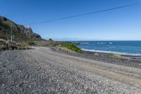 a gravel road going into the ocean with mountains in the background and a lighthouse to the left