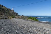 a gravel road going into the ocean with mountains in the background and a lighthouse to the left