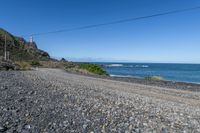 a gravel road going into the ocean with mountains in the background and a lighthouse to the left