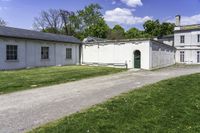 a white building with an arched doorway next to it on grass area with a paved pathway