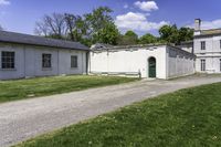 a white building with an arched doorway next to it on grass area with a paved pathway