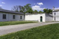 a white building with an arched doorway next to it on grass area with a paved pathway