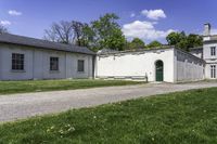 a white building with an arched doorway next to it on grass area with a paved pathway