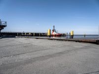 a man in black shirt standing on cement next to water and a yellow dock with red equipment