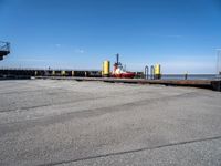 a man in black shirt standing on cement next to water and a yellow dock with red equipment