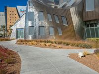 a building made of silver steel and rocks on the side of it, with some grass and bushes