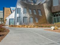 a building made of silver steel and rocks on the side of it, with some grass and bushes