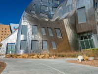 a building made of silver steel and rocks on the side of it, with some grass and bushes