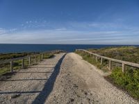 a gravel path with white pebbles and wood railings over looking the ocean and land