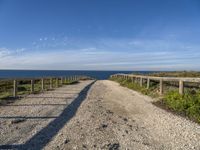 a gravel path with white pebbles and wood railings over looking the ocean and land