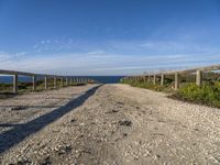 a gravel path with white pebbles and wood railings over looking the ocean and land