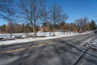 a car travels down an empty road with lots of snow on the ground and trees in the background