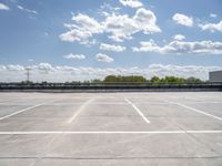 an empty parking lot, with some clouds in the sky behind it with a bench on the far side