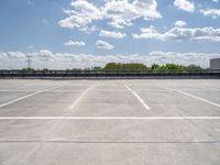 an empty parking lot, with some clouds in the sky behind it with a bench on the far side