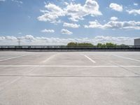 an empty parking lot, with some clouds in the sky behind it with a bench on the far side