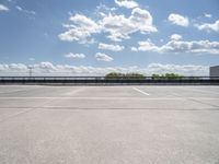 an empty parking lot, with some clouds in the sky behind it with a bench on the far side