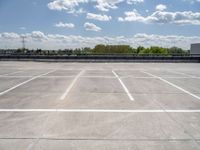 an empty parking lot, with some clouds in the sky behind it with a bench on the far side